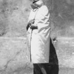 Black-and-white photo of a woman in elegant fashion, wearing a long coat, high heels, and a scarf.